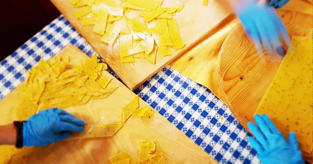 Details of the pasta making process showing a pair of hands cutting pasta dough into the right shapes